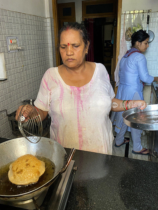 印度妇女穿着Salwar Kameez传统服装，在厨房柜台上的便携式煤气灶上照料karahi(印度炒锅)，印度早餐，普尔(poori)在沸腾的油中油炸，冒泡的食用油，不锈钢长柄勺蜘蛛丝